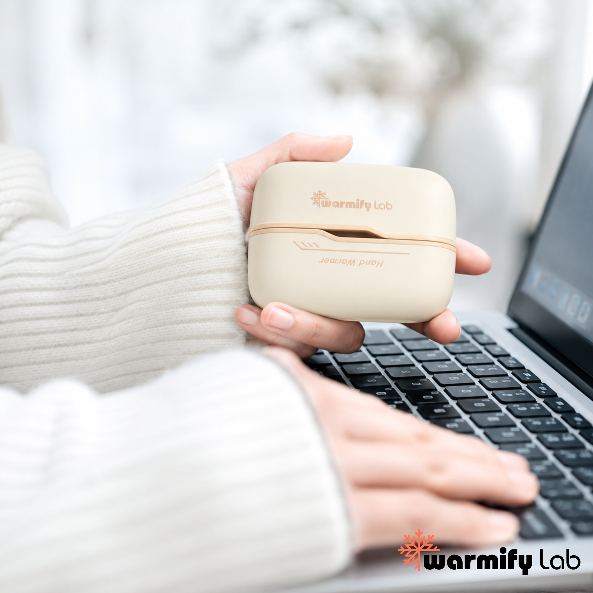 Person holding a Beige Rechargeable Hand Warmer by Warmify Lab in front of a laptop.